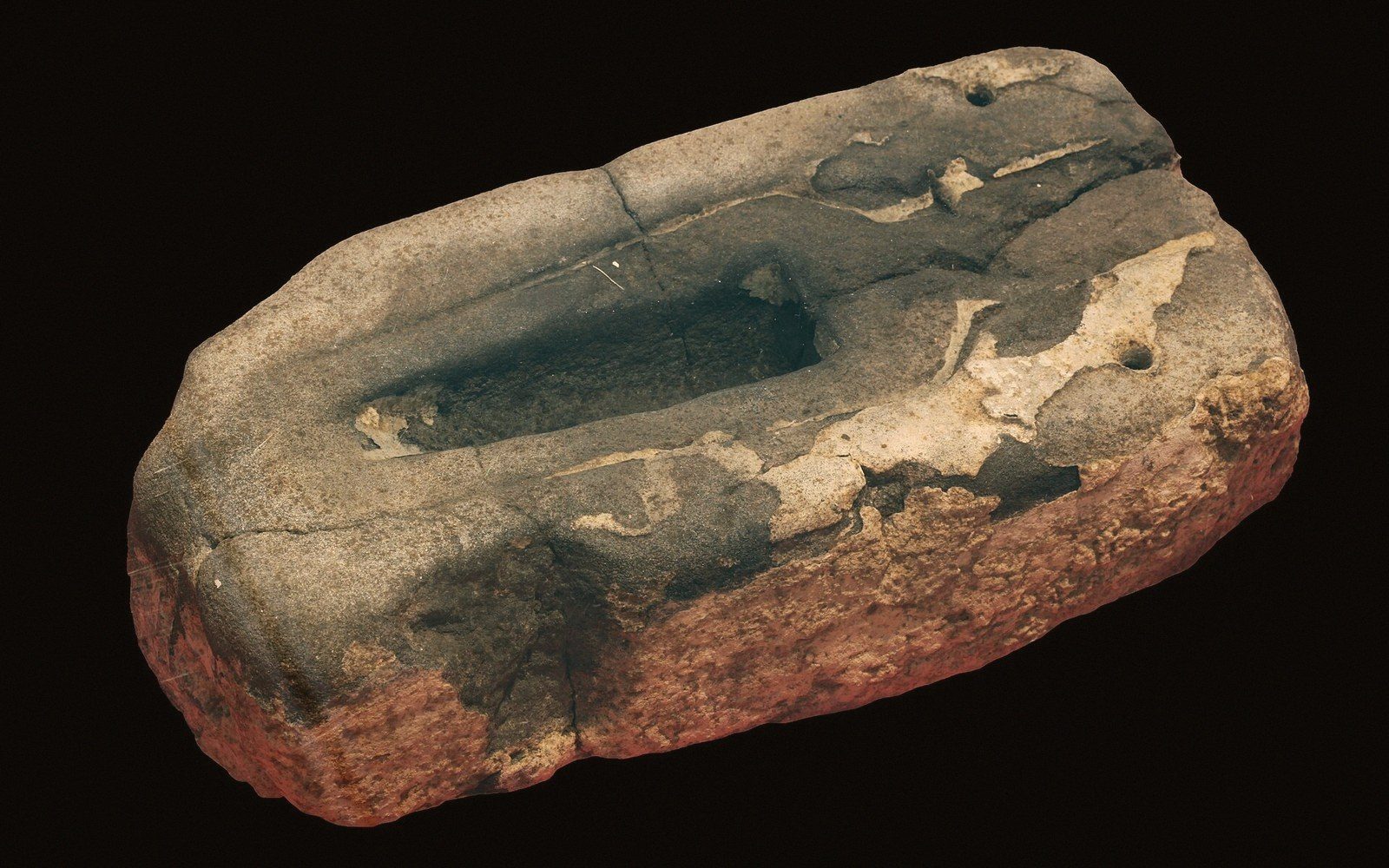 Ancient stone mould with a carved spear tip cavity, shown against a black background